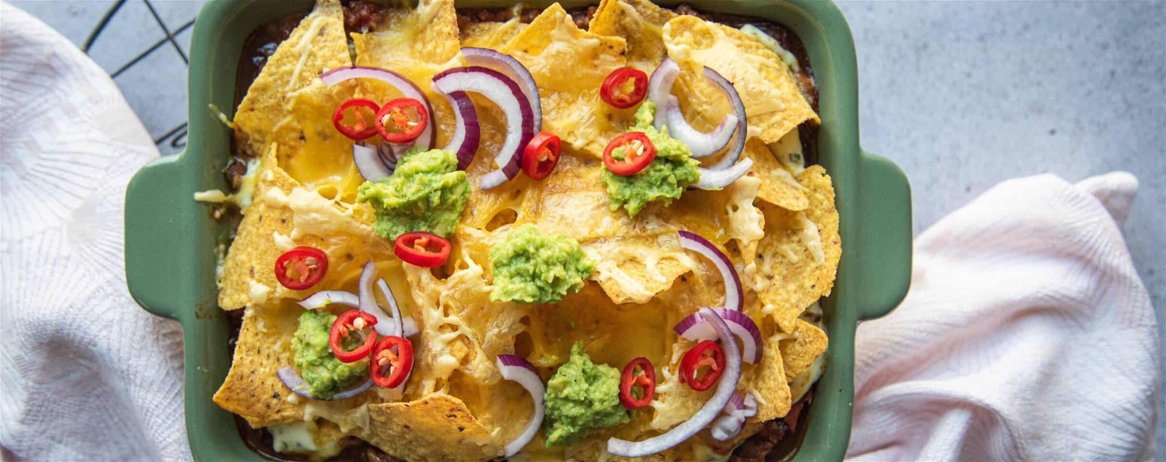 Nacho's ovenschotel met guacamole, gesmolten kaas, rode pepers en rode ui. Overheerlijk en gezond recept volgens de MA Methode.